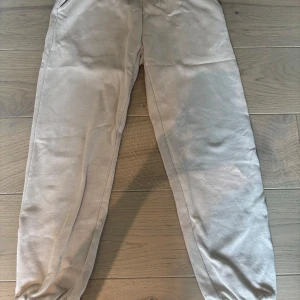 Beige mjukisbyxor från Today Tomorrow - Snygga beige mjukisbyxor från Today Tomorrow med resår i midjan och muddar vid bensluten. Tillverkade i mjukt bomullsmaterial, perfekta för chill dagar. Diskret logga på höften ger en clean look.