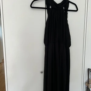 Svart långklänning Chiara Forthi - Supersnygg svart långklänning från Chiara Forthi med djup v-ringning och breda axelband. Klänningen har ett elegant fall och markerad midja, perfekt för dig som vill ha en stilren och chic look. Materialet känns mjukt och följsamt.
