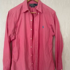 Rosa skjorta Polo Ralph Lauren M - Snygg rosa skjorta från Polo Ralph Lauren i slim fit-modell. Skjortan är i väldigt bra skick inga defekter. Skjortan har klassisk krage, långa ärmar och knäppning framtill. Ikoniska blå loggan broderad på bröstet. Perfekt för dig som gillar stilrena och färgstarka plagg. 