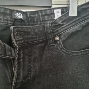 Svarta skinny jeans från Jack & Jones - Svarta jeans från Jack & Jones i storlek 176. Modellen är skinny fit med klassisk femficksdesign och dragkedja. Jeansen är tillverkade i stretchigt bomullsmaterial för en bekväm passform och har en stilren look som funkar till det mesta.