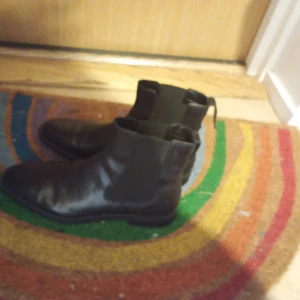 Svarta chelsea boots i skinn - Snygga svarta chelsea boots i skinn med klassisk rund tå och elastiska paneler på sidorna. Perfekta för dig som gillar stilrena och tidlösa skor med en clean vibe. Platt sula och enkel att dra på tack vare öglan bak.