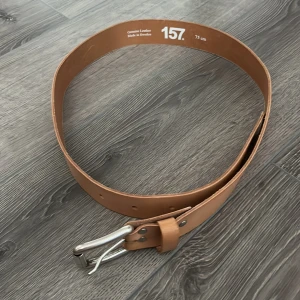 Brunt skärp i skinn - Snyggt brunt bälte i skinn från Lager 157, tillverkat i Sverige. Bältet har en klassisk design med silverfärgat spänne och flera hål för justering. Perfekt accessoar för att lyfta din outfit med en stilren touch. Aldrig använt!!