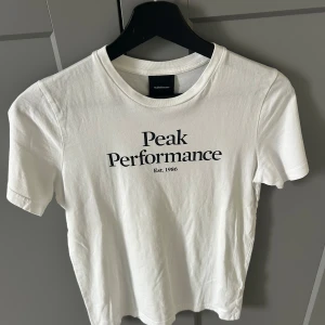 Vit Peak Performance t-shirt - Vit t-shirt från Peak Performance med svart logotyptryck på bröstet. Använder den aldrig har använt kanske 3 gånger därför jag säljer den. T-shirten är som helt ny. Storlek 160. Bara att skriva om det finns frågor eller om man vill ha mer bilder. Stryket tröjan innan jag skickar iväg den.