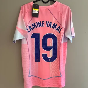 Barça Lamine Yamal rosa matchtröja Nike - Snygg FC Barcelona fotbollströja i rosa och ljusblått med Lamine Yamal och nummer 19 på ryggen. Tröjan har korta ärmar, Nike-logga, klubbmärke och Spotify-logga på bröstet. Tillverkad i lätt och ventilerande funktionsmaterial, perfekt för träning eller match.