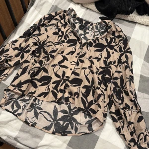 Beige blommig skjorta från Lindex XS - Snygg beige skjorta från Lindex i storlek XS med svart blommigt mönster. Skjortan har långa ärmar, knappar framtill och en avslappnad passform. Perfekt för dig som gillar en trendig och bekväm stil.