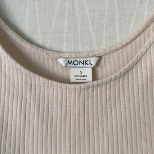 Beige ribbad linnetopp från Monki - Superenkel och snygg beige linnetopp från Monki i ribbad bomull. Croppad modell med breda axelband och rundad halsringning. Perfekt att styla med höga jeans eller kjol för en chill look.