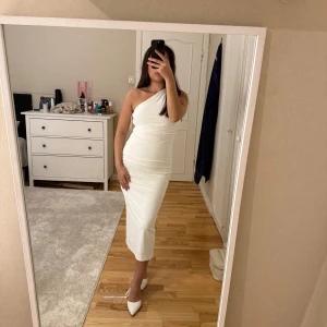 Vit one shoulder långklänning - Säljer en elegant vit långklänning med one shoulder-design. Klänningen har en figurnära passform och är helt ärmlös på ena sidan, vilket ger en stilren och modern look. Perfekt för dig som vill sticka ut med en enkel men snygg outfit.