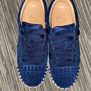 Blå Christian Louboutin sneakers med nitar - Snygga mörkblå sneakers från Christian Louboutin i mocka med nitar på tån och klassisk röd sula. Skorna har snörning och vit platt sula, perfekt för dig som vill sticka ut. Skorna är köpta för 8500 av privatperson och säljs för mer än 50% av skorna är dessutom bara använda 4 gånger och jag säljer dessa för att jag har ingen användning av de. Pris är ej hugget i sten
