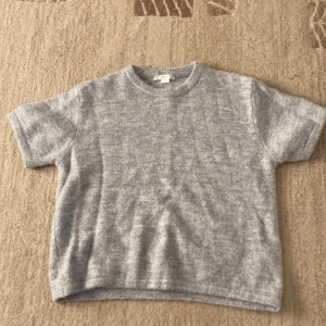 Grå stickad kortärmad tröja Gina Tricot - Supermjuk och enkel grå stickad tröja från Gina Tricot med korta ärmar och rund hals. Perfekt till jeans eller kjol för en chill och stilren look. Lätt oversized passform och ribbad kant vid halsen. Änvänd 1 gång 