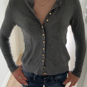Grå kofta med guldknappar - Snygg grå kofta med långa ärmar och stilrena guldknappar hela vägen framtill. Perfekt att slänga över en topp eller bära stängd. Mjuk och tunn, passar året runt och är lätt att matcha med jeans eller kjol.