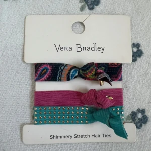 Färgglada hårsnoddar från Vera Bradley - Tre elastiska hårsnoddar från Vera Bradley i olika färger och mönster. En har paisleymönster i blått, rosa och orange, en är ceriserosa och en är turkos med små guldiga nitar och en liten guldcharm med VB-logga. Perfekt för att ge din frisyr extra färg och stil.