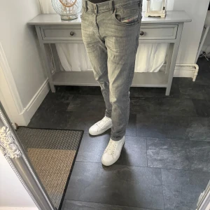 Grå Diesel Larkee jeans slim fit - Säljer ett par grå Diesel Larkee jeans med slim fit och klassisk femficksdesign. Jeansen har en snygg tvättad look, raka ben och svart läderpatch bak i midjan. Perfekta för dig som gillar stilrena och bekväma jeans med modern passform.