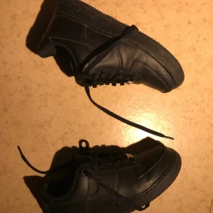 Svarta Nike Air Force sneakers - Snygga svarta Nike Air Force sneakers i skinn med klassisk design och snörning. Perfekta för en stilren look. De har en robust sula och ikonisk Nike-logga på sidan. Nästan aldrig använd och inga defekter. Priset kan jag diskutera