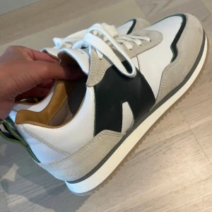 Alohas vita och grå sneakers med gröna detaljer - Snygga sneakers i vitt skinn med beige mockadetaljer och gröna inslag på sidorna. I väldigt fint skick. Använt 1 gång.