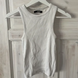 Vit ribbad linnetopp från Bik Bok - Säljer en vit ribbad linnetopp från Bik Bok i storlek M. Toppen är ärmlös med rund halsringning och har en tight passform. Perfekt att styla med jeans eller kjol för en clean och fräsch look.