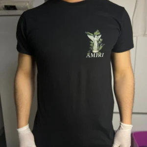 Svart Amiri t-shirt med ängeltryck - Svart t-shirt från Amiri med stort tryck av en ängel och gröna blad på ryggen samt mindre tryck på bröstet. Klassisk passform med rund hals och korta ärmar. Perfekt för dig som vill sticka ut med en unik design.