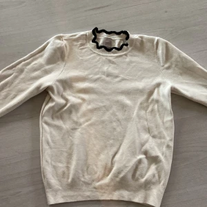 Vit tröja med volangkrage från H&M - Snygg vit långärmad tröja från H&M i mjuk bomullsmix. Tröjan har en unik volangkrage med svart kant som ger en cool kontrast. Perfekt för dig som vill ha en enkel men ändå speciell look. Normal passform och ribbade muddar.