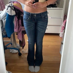 Blå bootcut jeans  - Säljer ett par blå jeans som har dekorativa fickor bak. Jeansen har låg midja och klassisk femficksdesign. Midjemått 36-37cm raktöver och innerbenslängden är ca 77cm och pssar på mig som är ungefär 162!