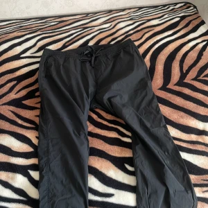 Svarta byxor med snörning - Svarta byxor med elastisk midja och snörning framtill. Lätta och bekväma, perfekta för chill dagar eller när du vill ha en avslappnad stil. Byxorna har fickor på sidorna och en bakficka. Materialet känns syntetiskt och är smidigt. Väldigt sköna passar jätte bra till träning och vanliga dagar där du bara vill chilla med dem. 