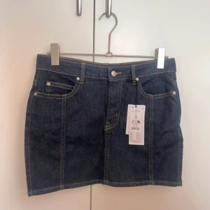 Gina tricot kjol  - Snygg mörkblå jeanskjol från Gina Tricot med klassisk femficksdesign, bälteshällor och kontrastsömmar. Kjolen är kort och har en rak passform som ger en cool och tidlös look. Perfekt att matcha med sneakers eller boots. Helt ny med prislapp 