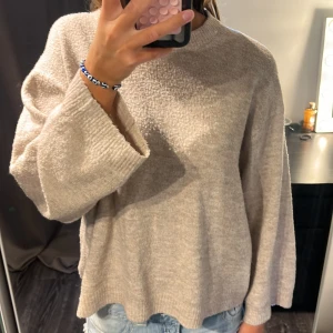 Beige stickad tröja från 157 - Mysig beige stickad tröja från 157 med rund halsringning och breda, långa ärmar. Tröjan har en loose passform och är perfekt för lager-på-lager. Enkel och stilren design som funkar till jeans eller kjol. Något nopprig 