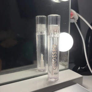 Sephora Glossed läppglans transparent - Säljer ett genomskinligt läppglans från Sephora Glossed-serien. Kommer i en stilren, rund tub med silvrig text och transparent plast. Perfekt för att ge läpparna en glansig finish utan färg. Enkel att ta med i väskan.