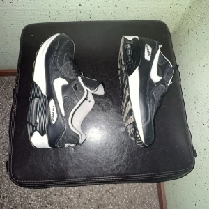 Nike Air Max 90 svart/vit sneakers - Snygga Nike Air Max 90 sneakers i svart, vitt och metallic silver. Klassisk chunky sula med synlig Air Max-dämpning, mesh och skinnpaneler samt vita detaljer och snörning. Perfekta för dig som gillar streetstyle och sportig vibe.