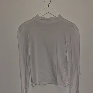 Vit långärmad topp från Zara - Säljer en stilren vit långärmad topp från Zara i storlek S. Toppen har lätt puffade axlar och en högre halsringning som ger en trendig look. Tillverkad i mjukt bomullsmaterial, perfekt för lager-på-lager eller som den är.