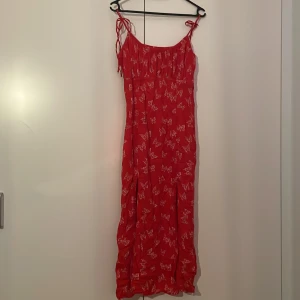 Röd långklänning med fjärilsmönster - Superfin röd långklänning med vita fjärilar och smala axelband som knyts. Klänningen har en luftig passform och är perfekt för varma dagar. Materialet känns lätt och flowy, och mönstret ger en söt och somrig vibe. Står medium men för mig som har större byst rekommenderar jag för dem som har lite mindre byst då den ger obehag i det området 