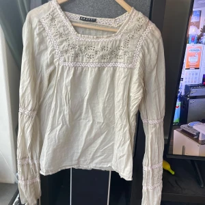 Beige blus med spets från Kaffe XL - Sönder vid ryggen! Supersöt beige blus från Kaffe i storlek XL. Blusen har långa ärmar, vackra spetsdetaljer och broderade partier både fram och på ärmarna. Tillverkad i ett lätt och luftigt bomullstyg, perfekt för vår och sommar. 