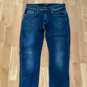 Replay Anbass jeans blå, stl 31 - Snygga Replay Anbass jeans i mörkblå tvätt med slitningar och klassiska kontrastsömmar. Modellen har fem fickor, dragkedjegylf och broderade bakfickor med Replay-logga. Perfekta för dig som gillar en modern och stilren look.