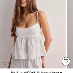 Vit linnetopp med knyt i ryggen - Superfin vit linnetopp med tunna axelband och volangig nederdel. Toppen har öppen rygg med snygg knyt och justerbara axelband. Perfekt för varma dagar och ger en luftig känsla. Materialet är lätt och har en naturlig struktur. Toppen är endast använd en gång!