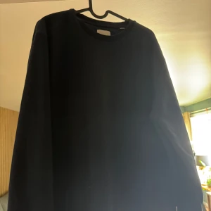 Mörkblå sweatshirt från Jack & Jones - En stilren mörkblå sweatshirt från Jack & Jones med rund hals och långa ärmar. Tröjan är enkel och passar perfekt till jeans eller joggers. Tillverkad i mjuk bomull för en skön känsla hela dagen.