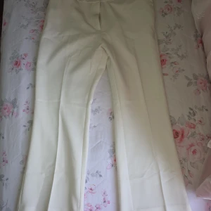 Vita kostymbyxor från H&M, strl 46 - Snygga vita kostymbyxor från H&M i storlek 46. Byxorna har raka ben och klassisk passform med pressveck. Perfekta för en clean och stilren look. Materialet känns mjukt och har en lätt glansig finish.