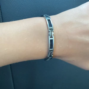Stilrent silverfärgat armband - Säljer ett coolt armband i silverfärg med svarta detaljer. Perfekt accessoar för dig som gillar en modern och clean look.