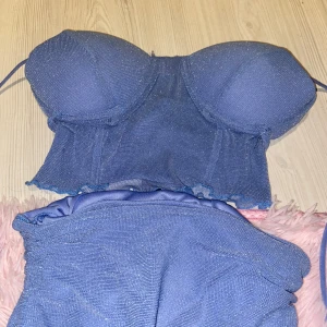 Glittrigt blått sett  - Säljer ett glittrigt blått sett. Säljs eftersom (som ni ser på bilden) det är alldeles för litet för mig. Toppen har vadderade kupor och är croppad med lätt transparent meshmaterial. Perfekt för dig som vill sticka ut med en snygg och trendig look nu i sommar. Styckpris (50 kr)