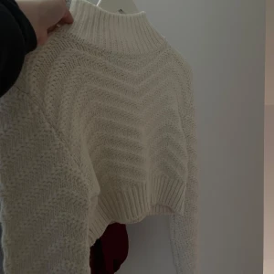 Vit croppad stickad tröja Chiquelle - Superfin vit stickad tröja från Chiquelle i croppad modell. Tröjan har ett snyggt mönster i stickningen, hög ribbad hals och långa ärmar. Perfekt att styla med höga jeans eller kjol för en trendig look.