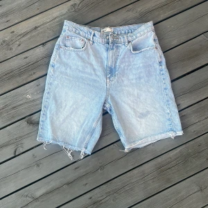 Ljusblå jeansshorts från Gina Tricot - Ljusblå jeansshorts från Gina Tricot med råa, fransiga benslut och klassisk femficksmodell. Shortsen är tillverkade i bomull och har en avslappnad passform med dragkedja och knapp framtill. Perfekta för sommardagar och enkel att matcha med allt. Högmidjade. 