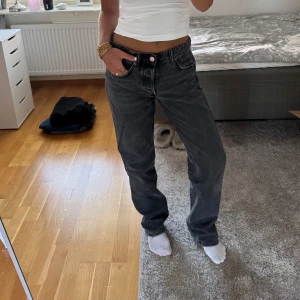 Svarta raka jeans från Zara - Säljer ett par svarta jeans från Zara med rak passform och klassisk femficksdesign. Jeansen har mid midja, knappgylf och är tillverkade i bomull. Perfekta för dig som gillar en avslappnad men stilren look. Säljer pga för stora, används inte längre. De är lite grå/svarta.