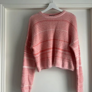 Rosa stickad tröja från Cotton Candy LA - Superfin rosa stickad tröja från Cotton Candy LA i croppad modell. Tröjan har ett randigt mönster i olika nyanser av rosa och vitt, med lång ärm och rund halsringning. Perfekt för dig som gillar en söt och trendig look.