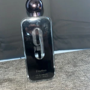 Divloo 9pm Eau de Parfum 100ml - Snygg parfymflaska från Divloo, 9pm Eau de Parfum, 100 ml. Flaskan är rektangulär med rund svart kork och har en stilren svart och silver design. Perfekt för dig som gillar moderna och eleganta dofter. Det finns kvar ungefär 97ml och är knappt använd