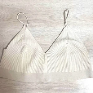 Ribbad  topp med smala band -  Ribbat topp i creme beige med smala axelband och v-ringning. Toppen är croppad och har en bredare resår nedtill.