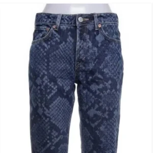 Blå bootcut jeans med ormmönster - Snygga blå jeans med snygg passform och coolt ormmönster. Jeansen har klassisk femficksdesign och stängs med knapp och dragkedja.