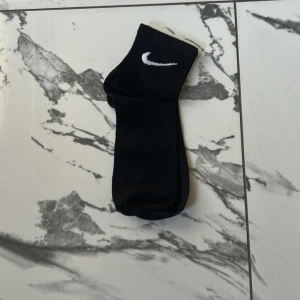 Svarta Nike strumpor med logga - Svarta strumpor från Nike med klassisk vit swoosh-logga upptill. Perfekta till sneakers och streetwear, i mjukt och bekvämt material som andas. Stilrena och passar till de flesta outfits. 5 pack för 100kr