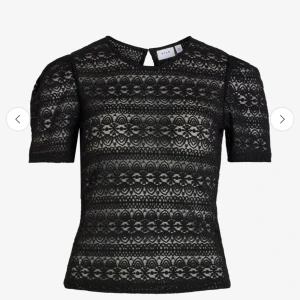 Svart spetsblus från Vila - Supersnygg svart blus från Vila i genombruten spets med blommigt mönster. Kortärmad modell med rund halsringning och knappdetalj i nacken. Perfekt för dig som vill ha en feminin och trendig look.