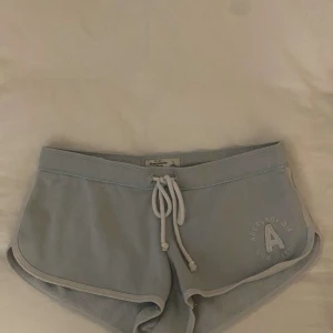 Ljusblå shorts  - Supermjuka och korta ljusblå shorts från Abercrombie & Fitch med vit snörning i midjan och broderad logga på ena benet. Sportig och avslappnad modell med vita kanter, perfekta för chill dagar eller träning.