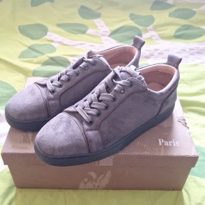 Grå mockasneakers från Louboutin - Snygga grå sneakers i mocka från Christian Louboutin med klassisk röd sula och svarta detaljer. Skorna har rund tå, platt sula och snörning. Perfekta för dig som vill ha en stilren men ändå lyxig look.