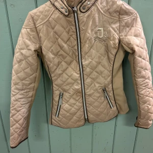 Beige quiltad stalljacka från Jacson - Snygg beige quiltad stalljacka från Jacson med dragkedja framtill och två dragkedjefickor. Jackan har hög krage med tryckknappar och broderad J-logga på bröstet. Perfekt för dig som gillar stilren och sportig look. Storlek 150cm