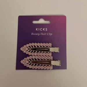 Rosa hårklämmpr från Kicks - Två snygga hårklämmor från Kicks dekorerade med ljusrosa pärlor och små glittriga stenar. Klämmorna har en spetsig form och metallfäste som håller håret på plats. Perfekt accessoar för att ge frisyren en söt och trendig touch eller att ha medan du sminkar dig🩷 Oanvända!