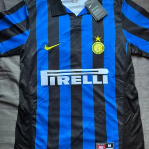 Inter Milan randig fotbollströja Nike  - Inter Milan fotbollströja från Nike i klassiskt blått och svart randigt mönster. Tröjan har korta ärmar, gul Nike-logga och klubbmärke med stjärna på bröstet. Pirelli som sponsor framtill. Tillverkad i lätt och ventilerande material.